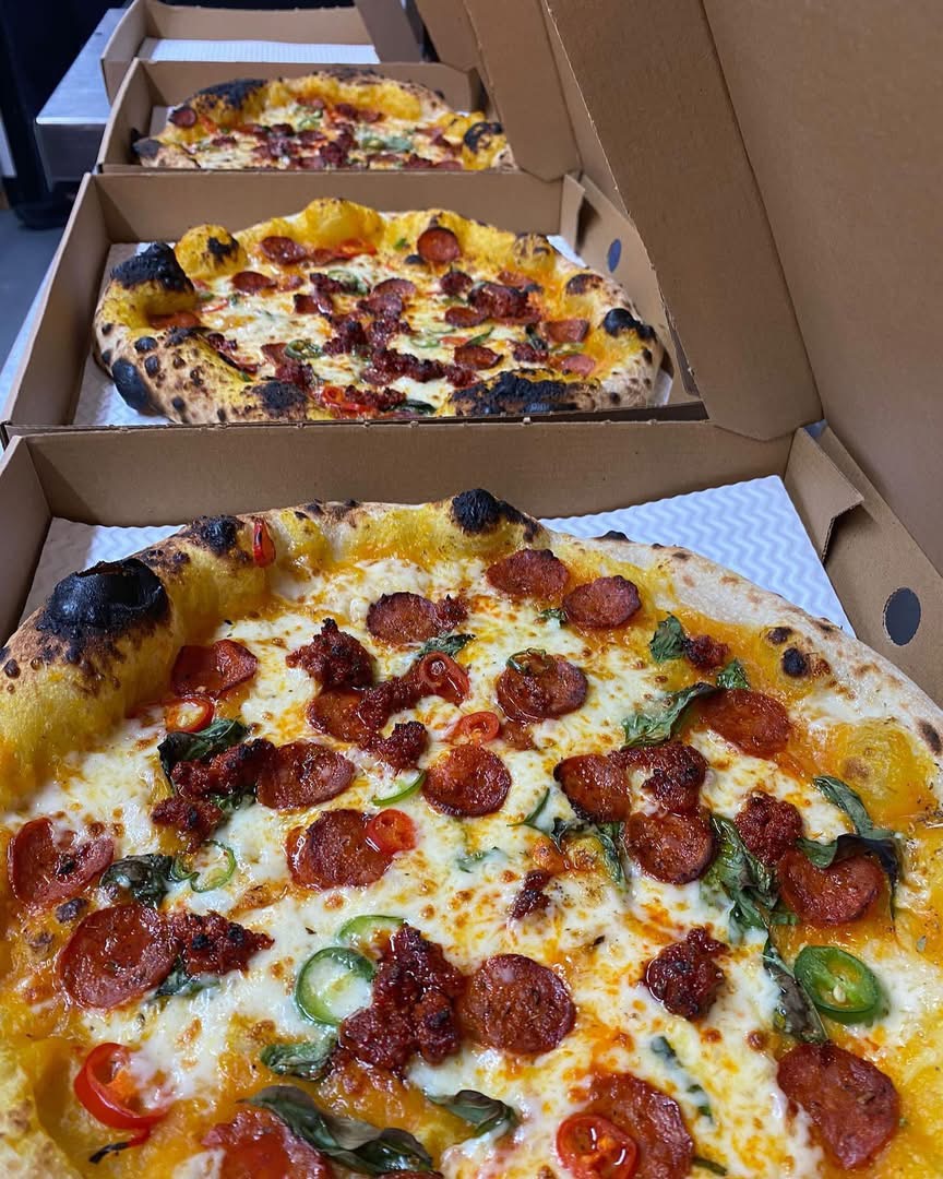 Three freshly baked pizzas in boxes for collection
